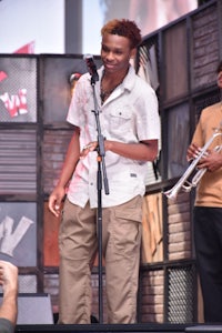 a man in a tan shirt standing in front of a microphone