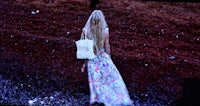 a woman in a floral dress walking through the sand