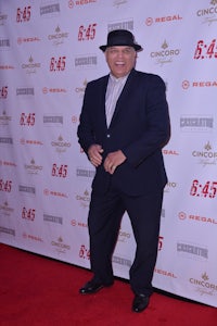 a man in a suit and hat standing on a red carpet