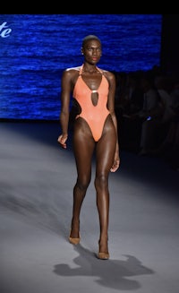 a black woman wearing an orange swimsuit on the runway