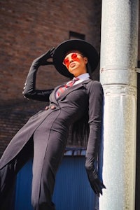 a woman in a black suit leaning against a pole