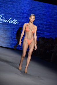 a woman in an orange bikini walks down the runway