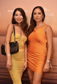 two women in orange dresses standing next to each other on a red carpet