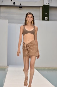 a model walks down a runway in a tan bikini and shorts