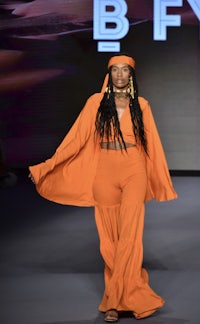 a woman wearing an orange outfit on the runway