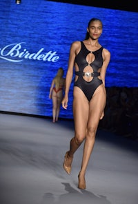 a model walks the runway wearing a black swimsuit