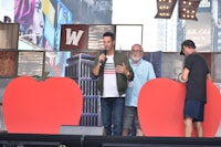 a man is standing on a stage in front of red hearts