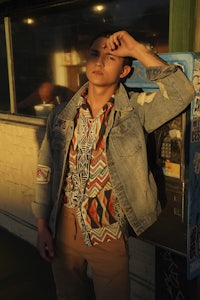 a young man in a denim jacket leaning against a phone booth