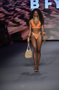 a black woman in an orange bikini walks the runway