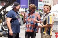 three men talking on a street in front of a camera