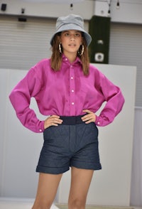 a woman in a pink shirt and denim shorts posing on a runway