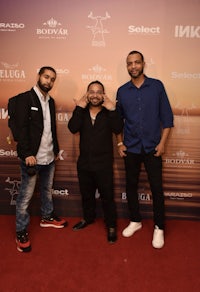 three men standing next to each other on a red carpet