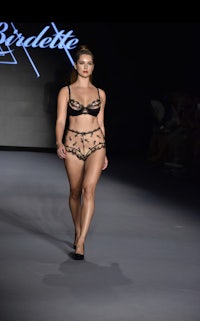 a model walks down the runway in a black and gold lingerie