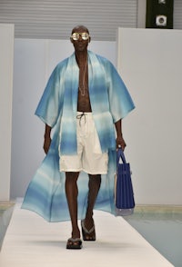 a man walking down the runway in a blue kimono and shorts