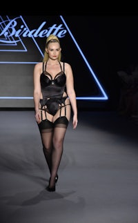 a woman in a black linger and stockings walks down the runway