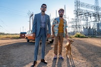 two men standing in front of a car with a dog