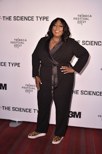 a woman in a black jumpsuit standing on a red carpet