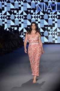 a model walks down the runway in an orange dress