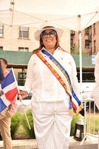 a woman in white with a hat and sash holding a flag