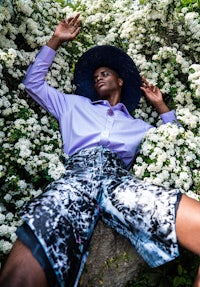 a black man laying in a field of flowers wearing a hat and shorts