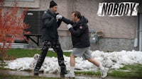 two men are fighting in front of a house