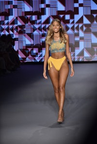 a model walks down the runway in a yellow bikini