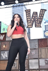 a woman in a red top and black pants is standing in front of a sign