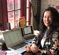 a woman sitting at a desk with two laptops in front of her