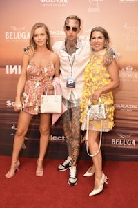 three women standing on a red carpet with purses