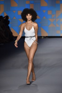 a model walks down the runway in a white swimsuit