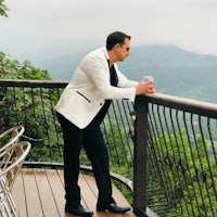 a man in a white tuxedo standing on a balcony overlooking the mountains