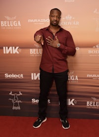 a man in a maroon shirt standing on a red carpet