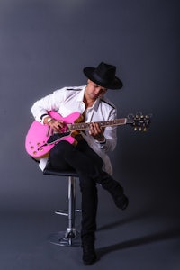 a man in a hat playing a pink guitar