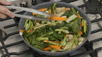 a person is slicing vegetables in a bowl on a stove