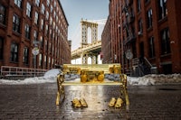 a gold bench in front of the brooklyn bridge