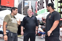 three men talking to each other on a street in times square