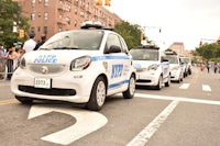 a group of smart cars parked on a street in front of a crowd of people