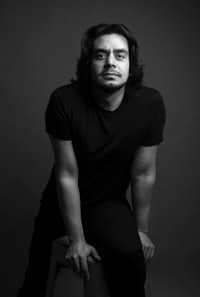 a black and white photo of a man posing on a stool