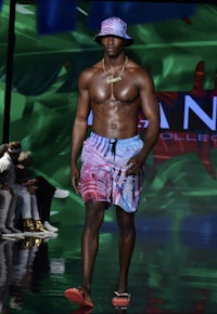 a male model walks the runway wearing colorful shorts and a hat