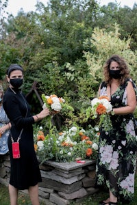 two women wearing face masks standing in a garden with flowers