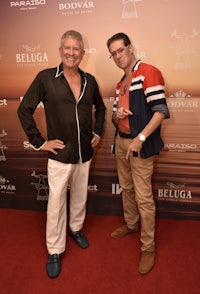 two men standing next to each other on a red carpet