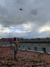 a woman is standing on a rooftop looking at a drone