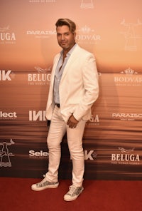 a man in a white suit standing on a red carpet