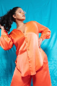 a woman in an orange shirt and pants posing on a blue background