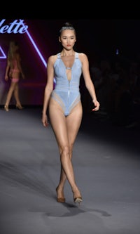 a woman in a blue swimsuit walks down the runway