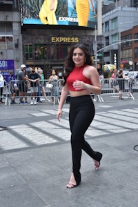 a woman in a red top and black pants walking down the street