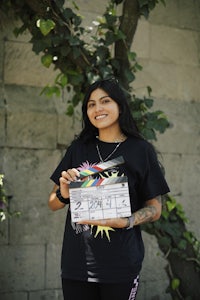 a woman holding a clapper board in front of a tree