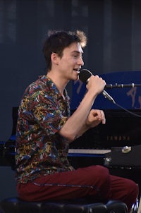 a young man singing into a microphone at a piano