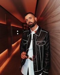 a man in a leather jacket leaning against a wall