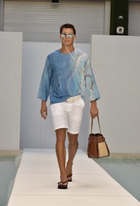 a man in white shorts and a blue shirt walking down the runway